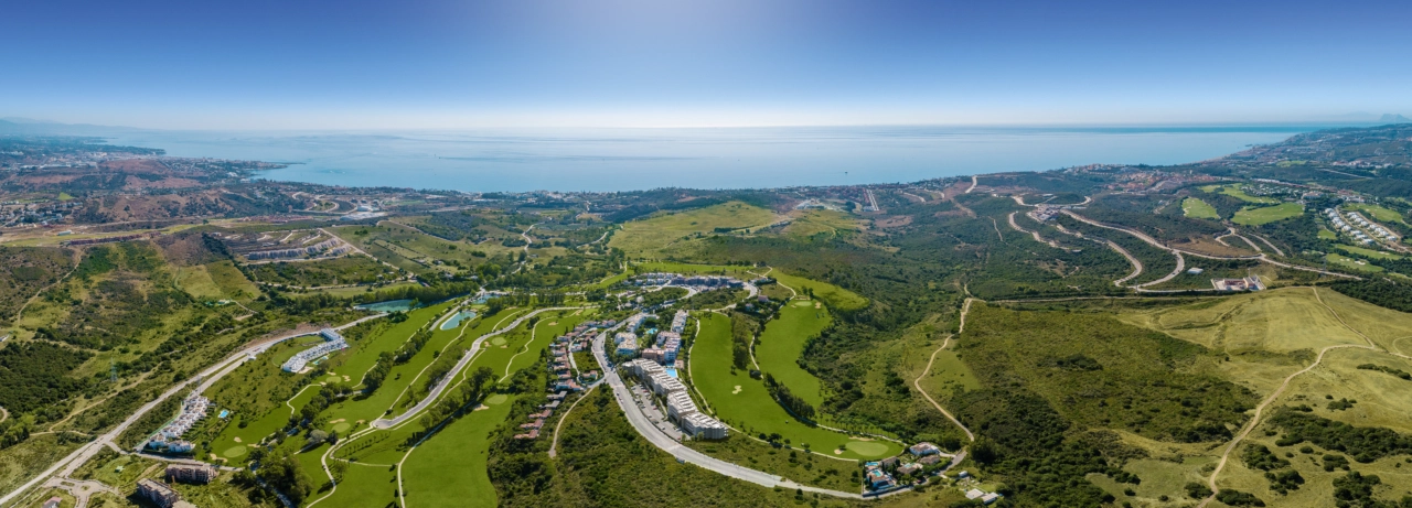 Eine weitläufige Luftaufnahme der Sunny Golf Anlage, perfekt integriert in die üppig grünen Fairways von Estepona Golf und das glitzernde Mittelmeer dahinter.